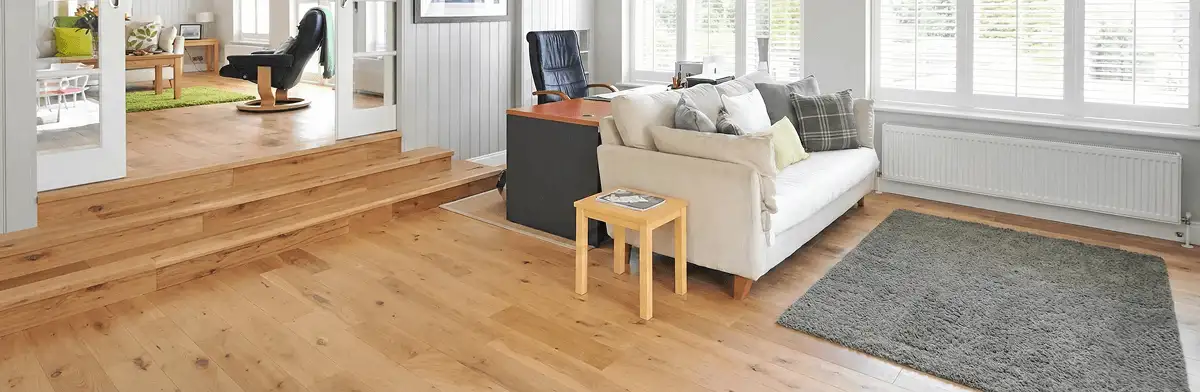A modern living room with professionally installed laminate flooring, a beige sofa, a small side table, a gray rug, and large windows with white shutters in Saint Louis, MO
